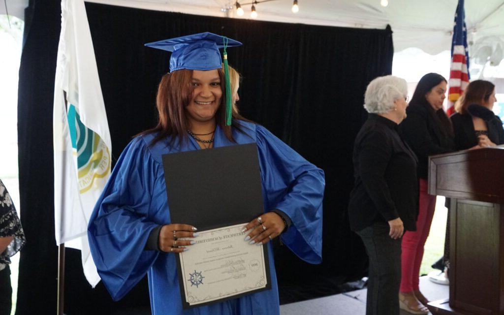 Smiling woman proudly showing her diploma in her graduation cap and gown