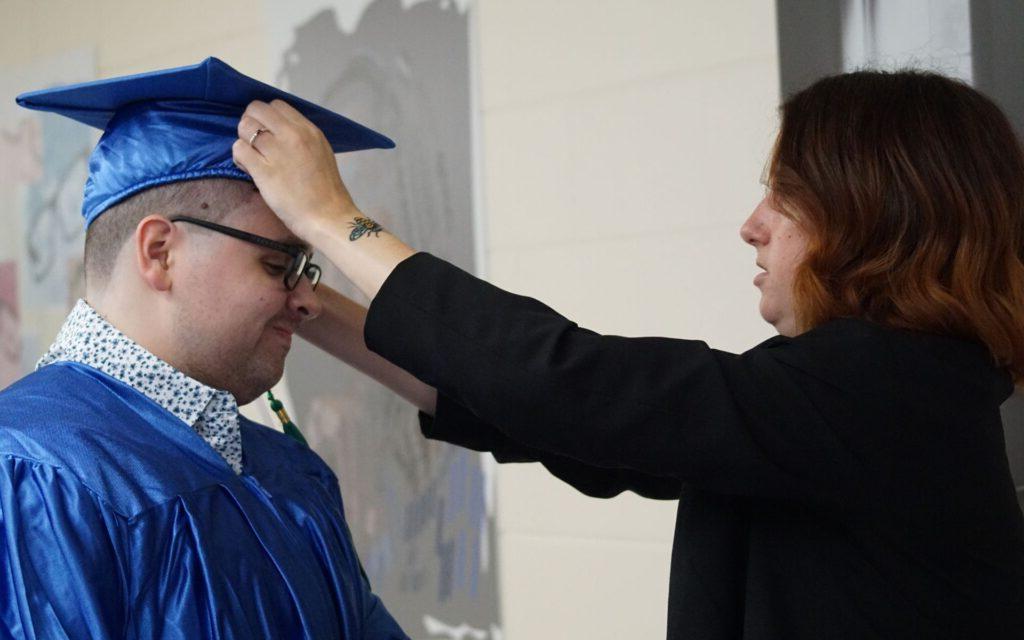 Graduate Nicolas Pinero Mortarboards getting his cap adjusted by a woman at graduation.